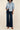 Person wearing a light blue denim shirt and dark blue jeans on a beige background
