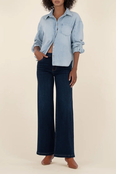 Person wearing a light blue denim shirt and dark blue jeans on a beige background