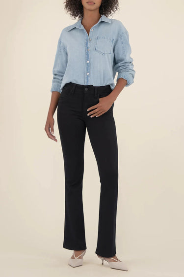 Person wearing a light blue denim shirt and black pants on a beige background