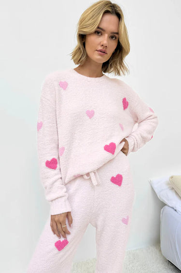Woman wearing a pink pajama set with heart patterns on a light background