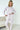Woman wearing a white pajama set with heart patterns in a minimalistic room.