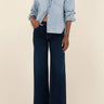 Person wearing a light blue denim shirt and dark blue jeans on a beige background