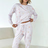 Woman wearing a white pajama set with heart patterns in a minimalistic room.