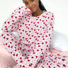 Person wearing a white hoodie with red heart patterns and matching pants on a pink bed.